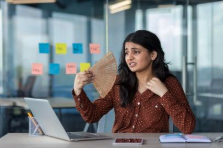Woman at her desk fanning herself to cool down during a hot flash