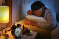 Woman asleep with a sleep mask next to an alarm clock on the nightstand